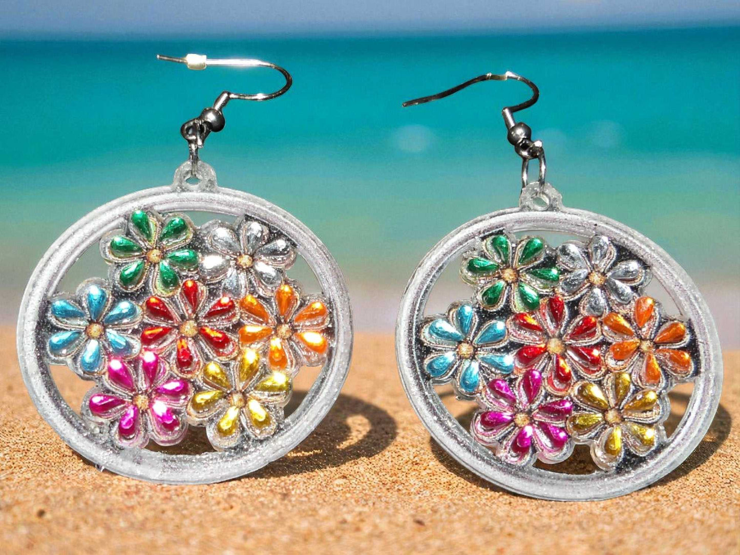 Handmade colorful flowers earrings with vibrant petals in a silver circular frame on a sandy beach background