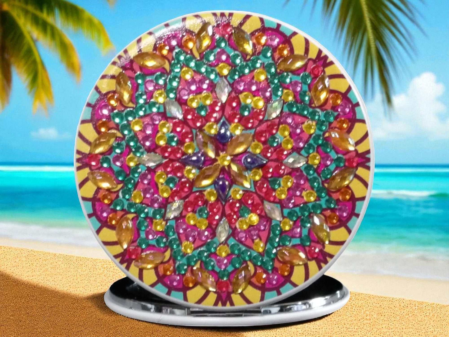 Colorful round pocket mirror with vibrant mandala design and gemstones on beach background