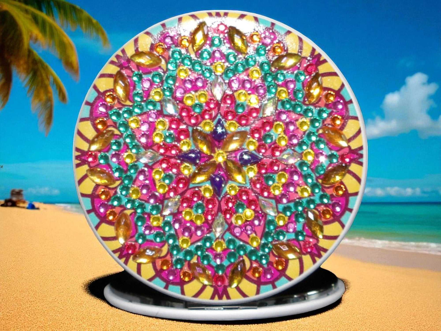 Colorful round pocket mirror with mandala design featuring magnification and regular mirror sides on a beach background
