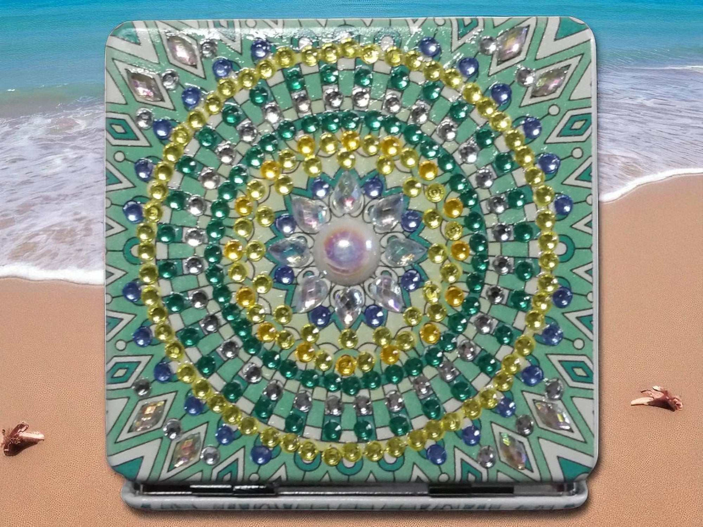 Green square pocket mirror with mandala design and decorative beads on beach background