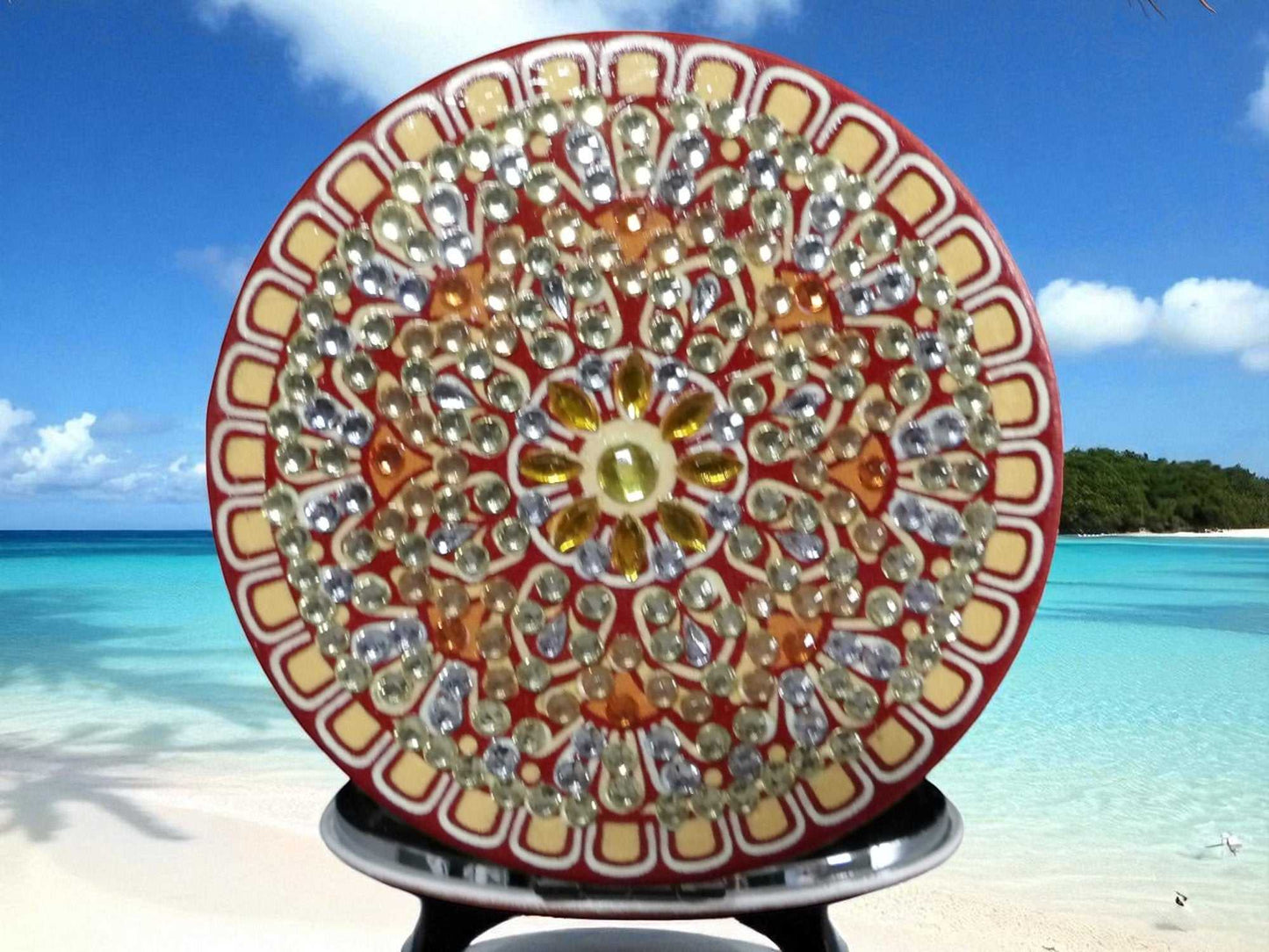 Brown round pocket mirror with intricate mandala design and decorative stones on beach background