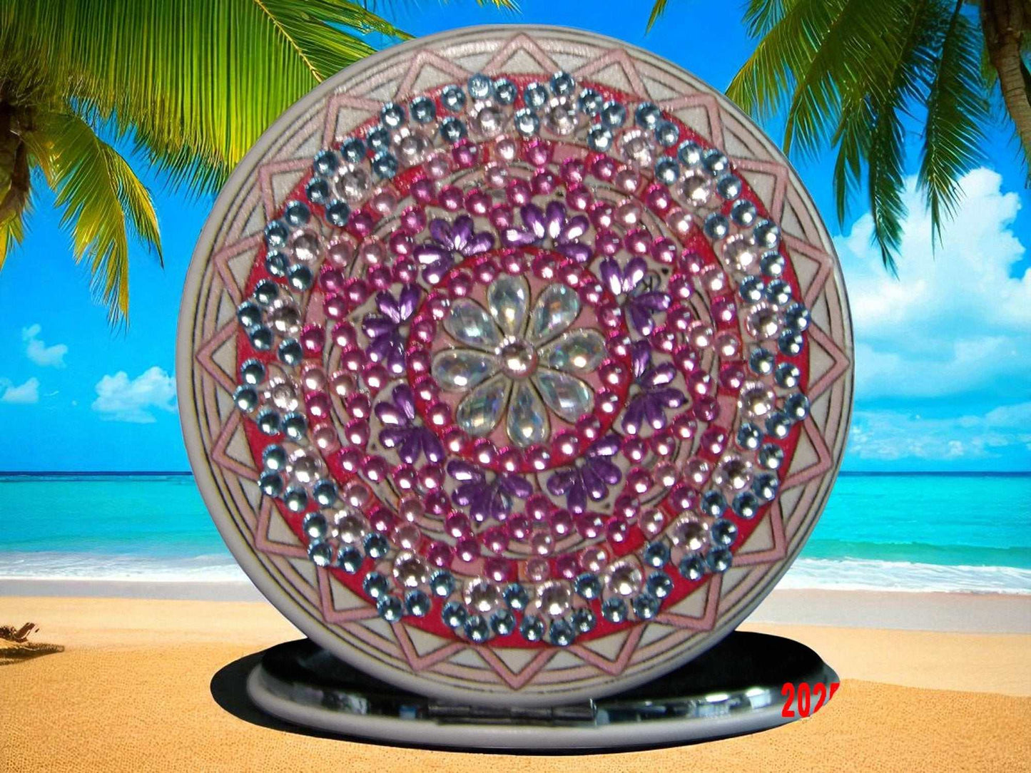 Pink purple blue round pocket mirror with mandala design and magnification on one side, set against a beach background
