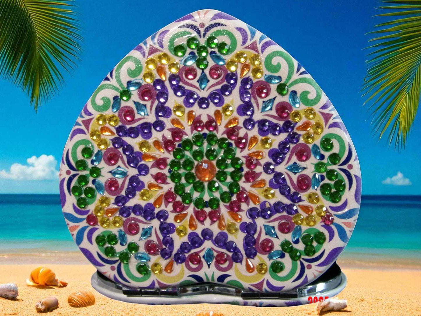 Purple and green heart shaped pocket mirror with colorful mandala design on beach background