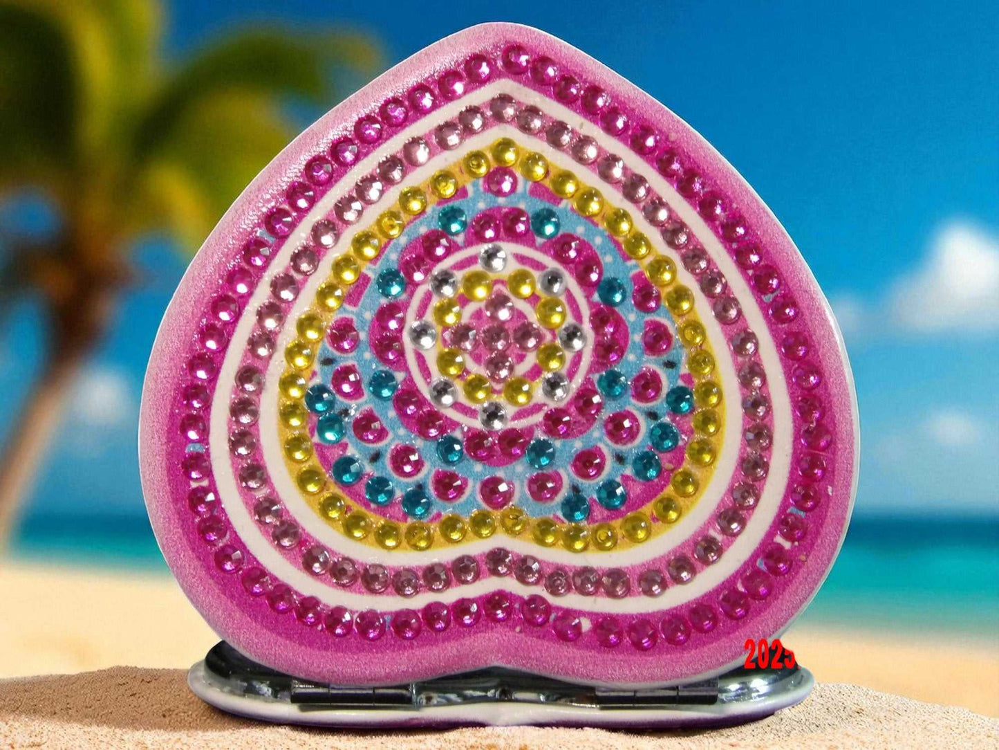 Pink and yellow heart shaped mandala pocket mirror with magnification and regular side on sandy beach background