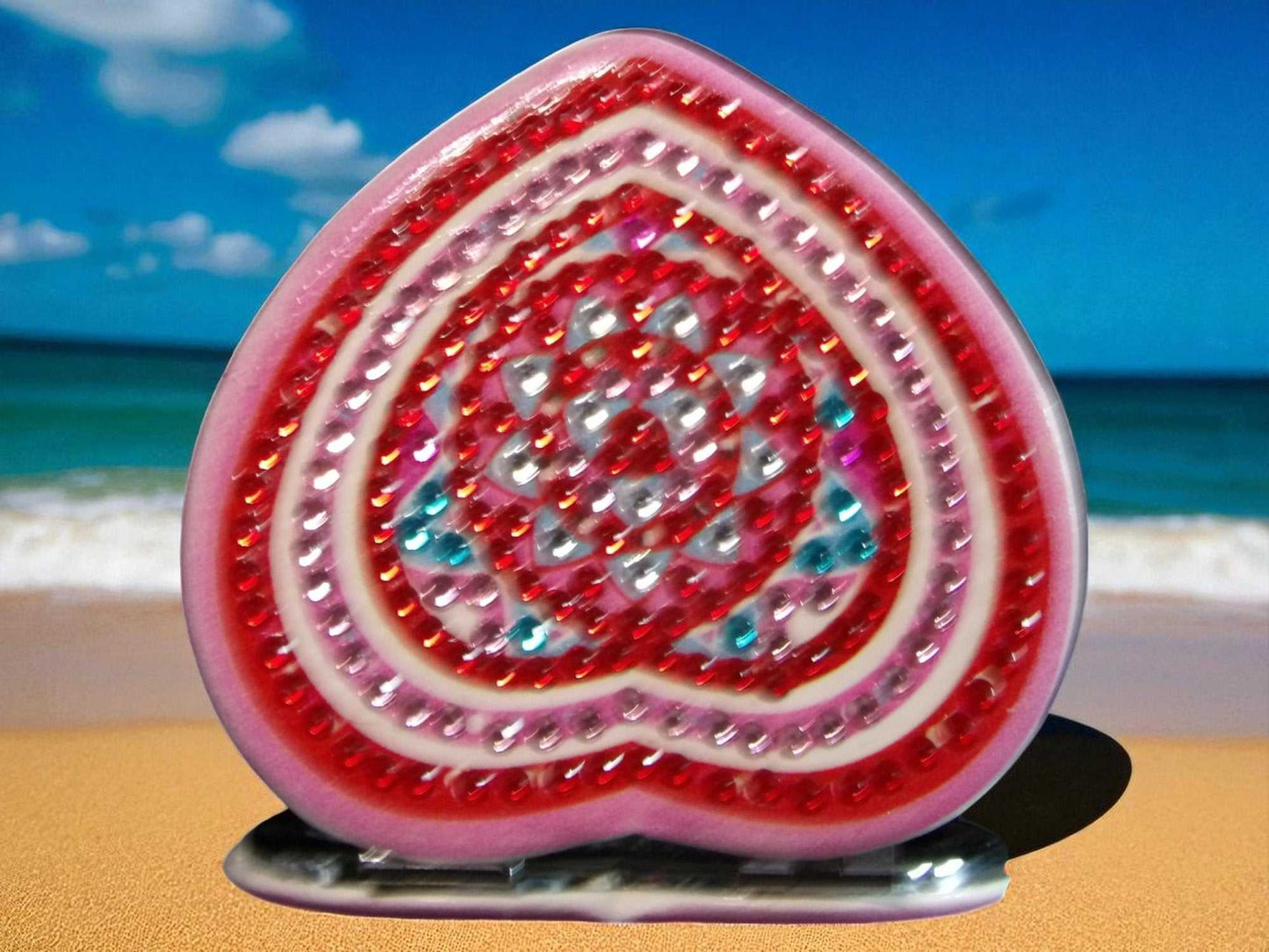 Pink and red heart-shaped mandala design pocket mirror with magnification and regular mirror sides on beach background