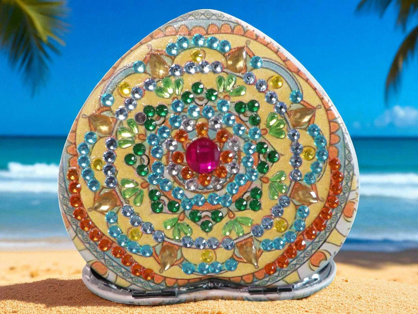 Gold heart shape pocket mirror with colorful mandala design and gemstone accents on beach background