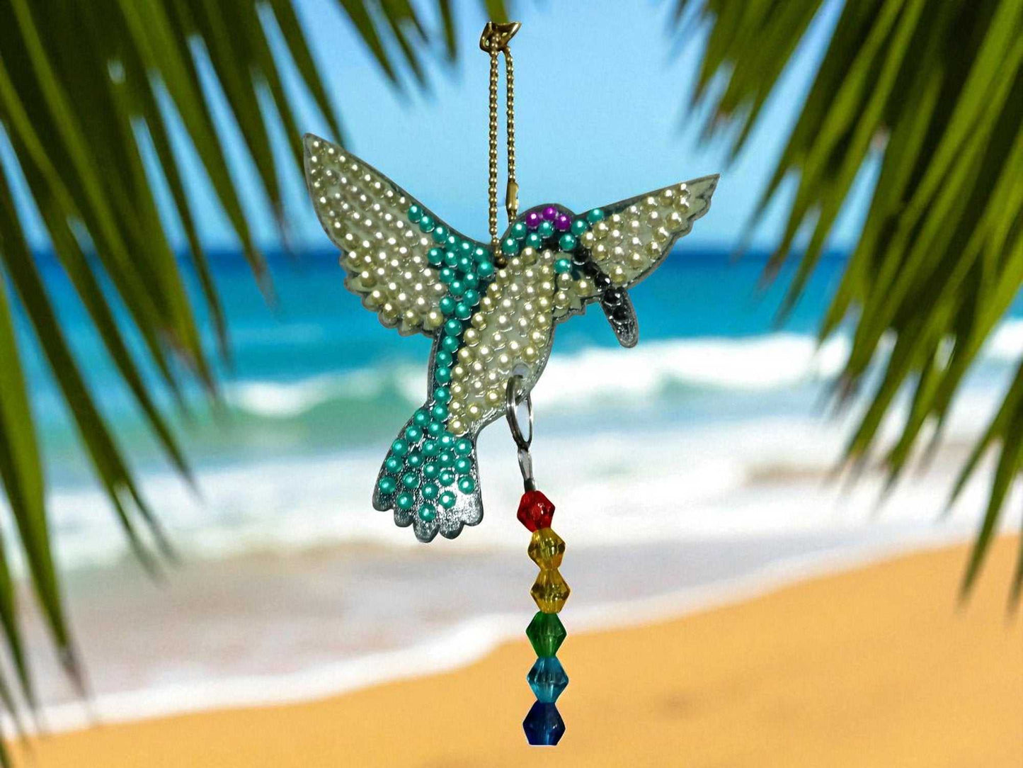 Blue & White Hummingbird sun and wind catcher hanging on a beach background with palm leaves