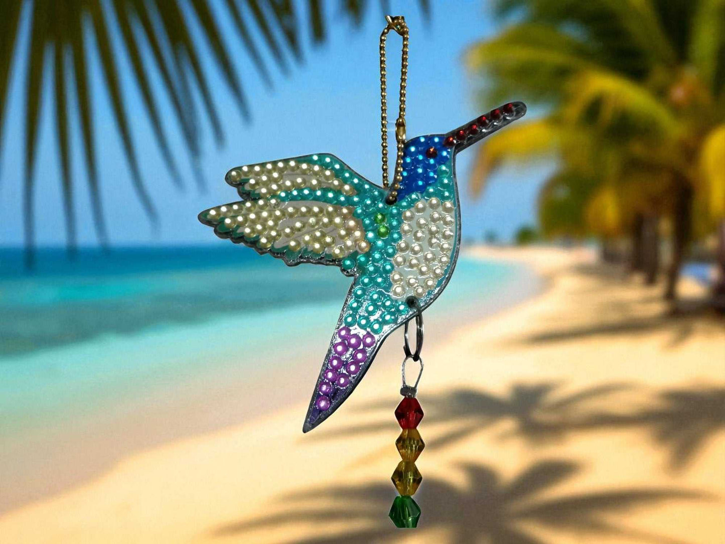 Blue white purple hummingbird sun wind catcher hanging outdoors by the beach with palm trees background