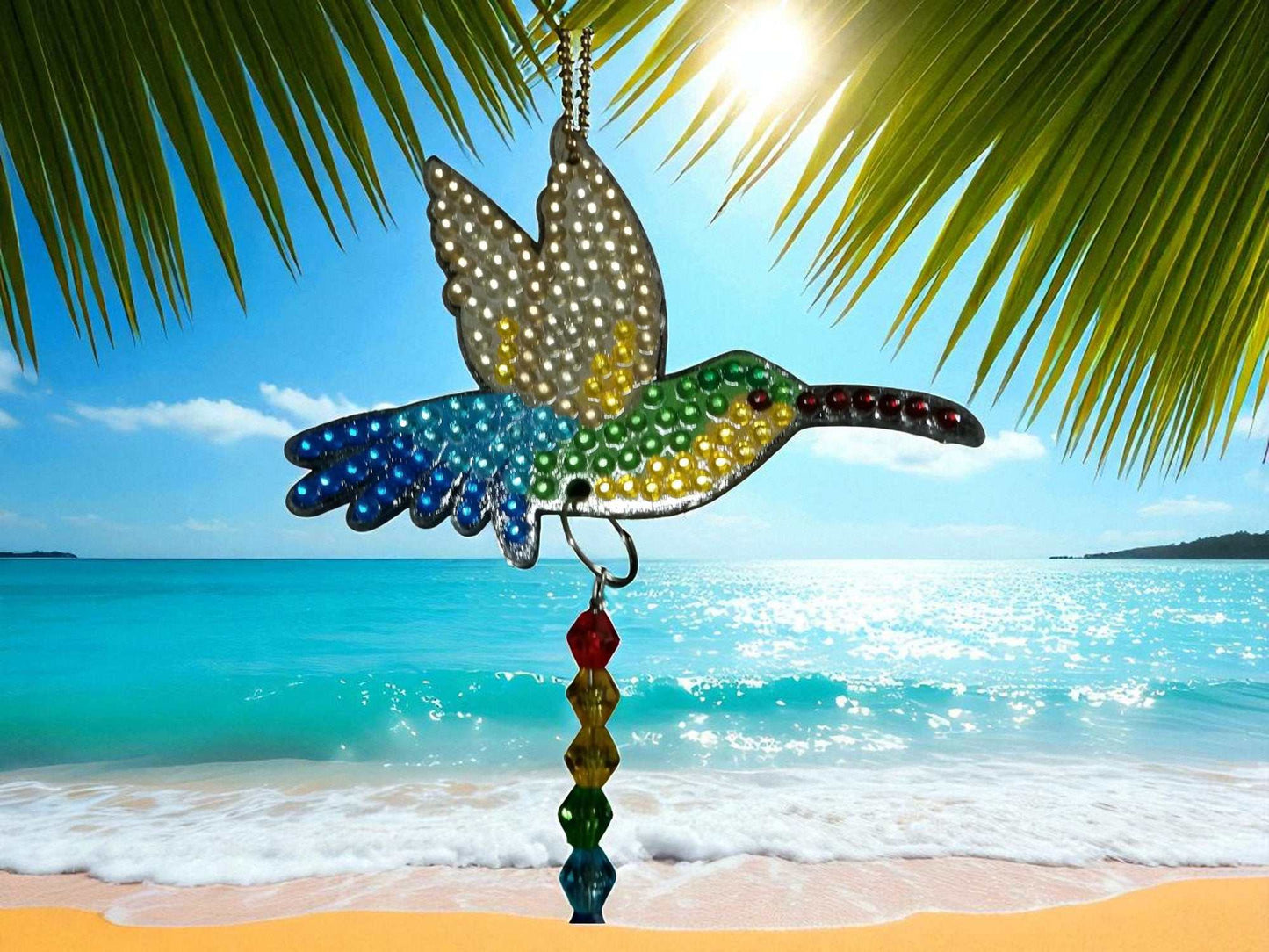 Multi-colored hummingbird sun catcher hanging outdoors by the beach under palm leaves