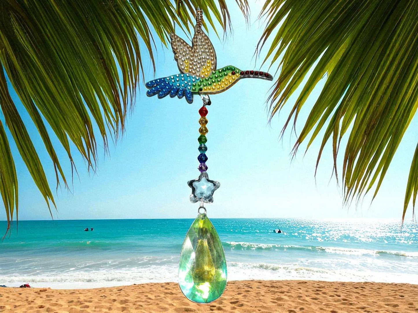 Multi-colored hummingbird sun and wind catcher hanging outdoors by the beach under palm leaves
