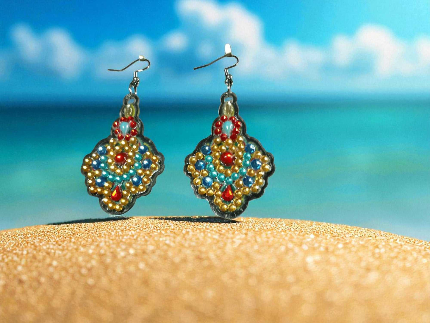 Blue and gold colorful handmade earrings on sandy beach with ocean background