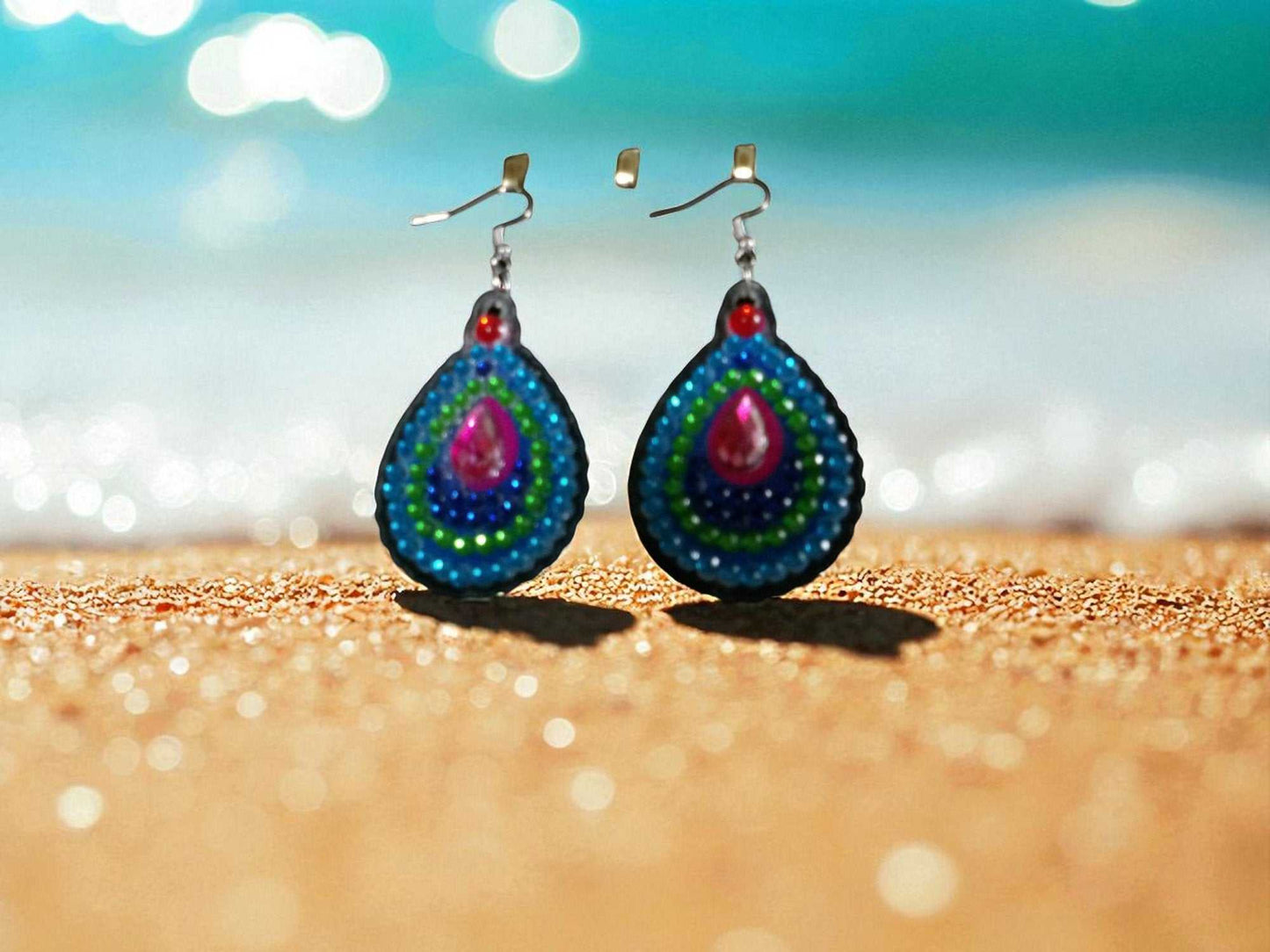 Blue green round handmade earrings with vibrant beaded patterns on sandy surface