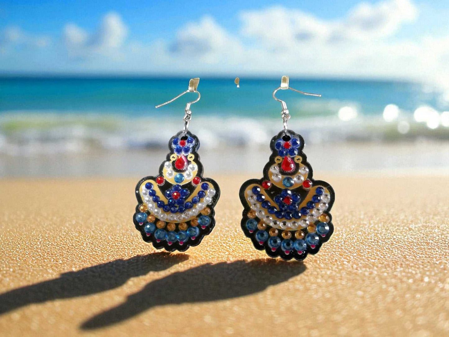 Handmade blue and yellow beaded earrings displayed on sandy beach background