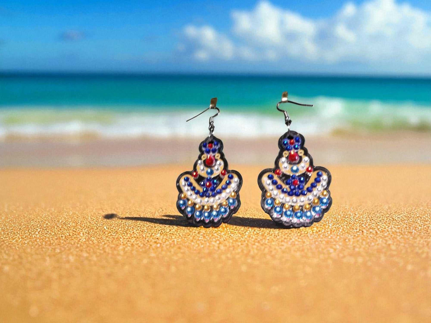 Blue and yellow handmade earrings with bead detailing on sandy beach background
