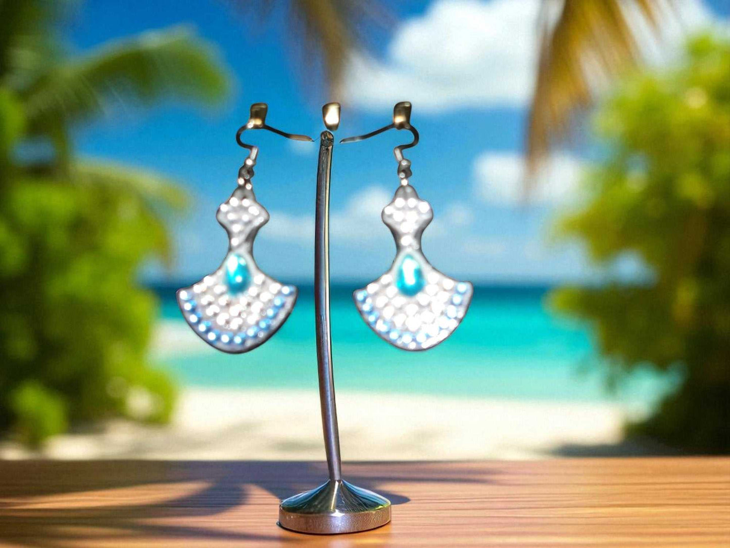 Blue & crystal swing earrings with unique handmade design displayed on stand at beach background