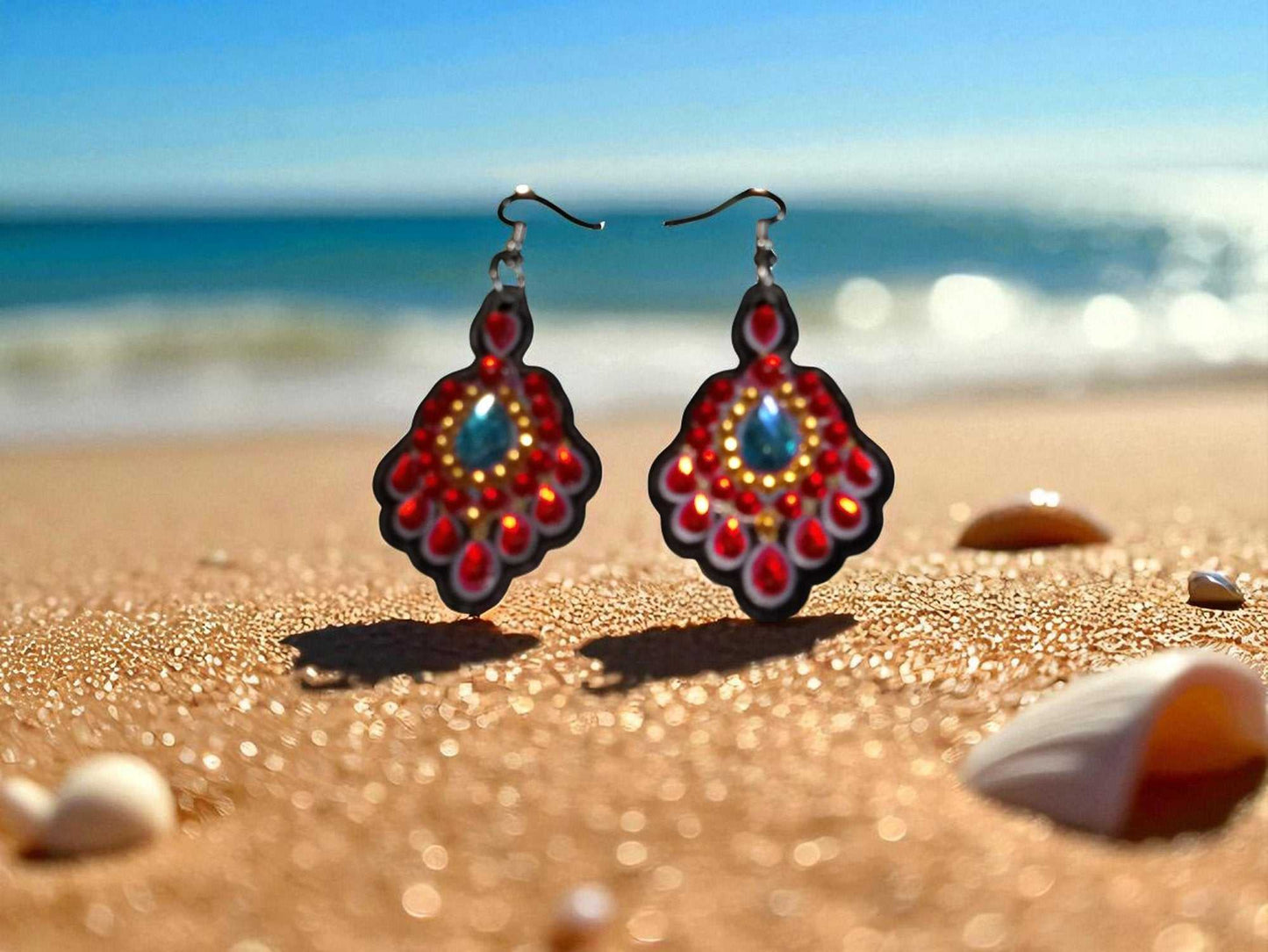 Red and blue crystal earrings on sandy beach with seashells background
