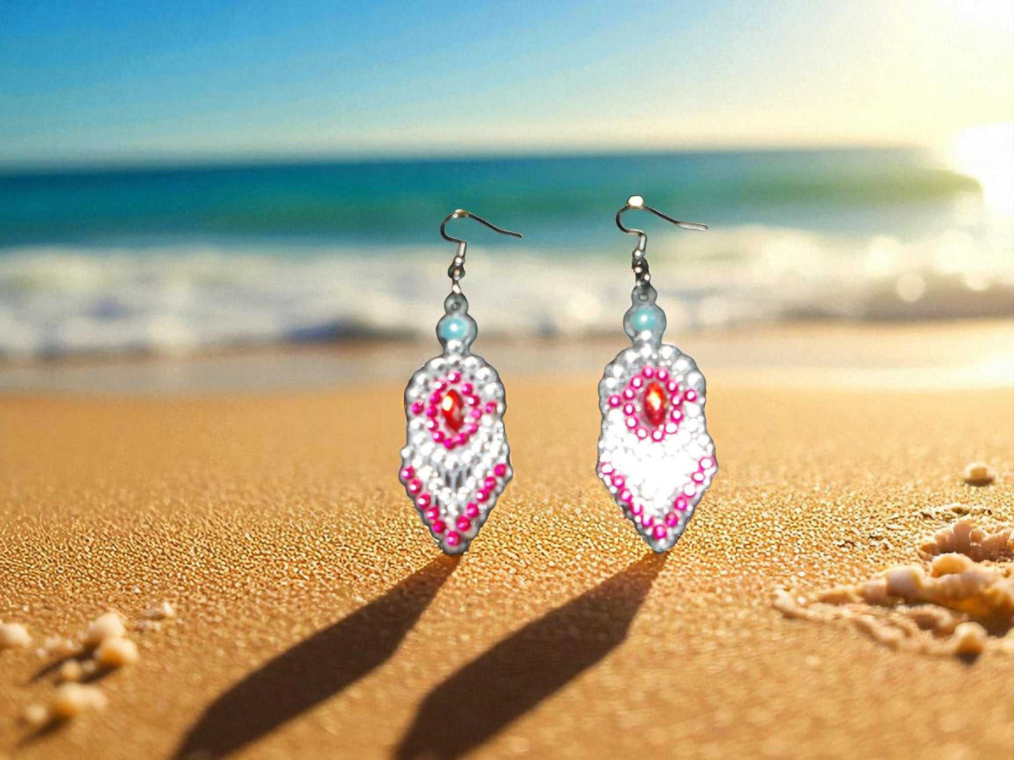 Red and blue beaded pearl earrings on sandy beach background