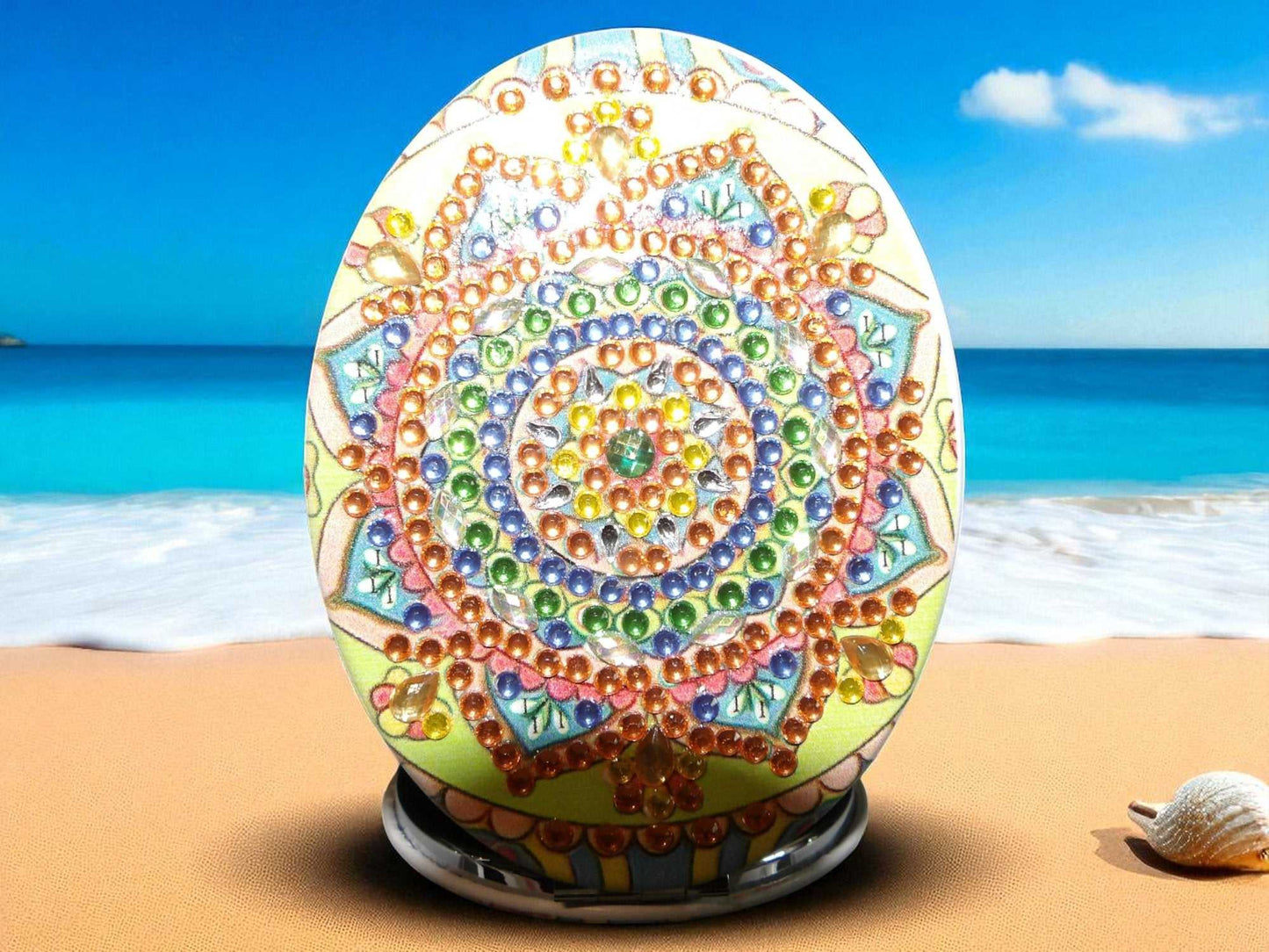Golden oblong pocket mirror with colorful mandala design and magnification feature on beach background