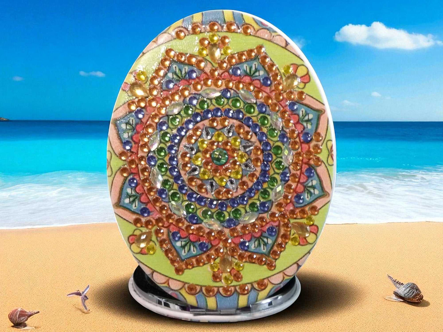 Golden oblong pocket mirror with colorful mandala design and magnification feature on beach background