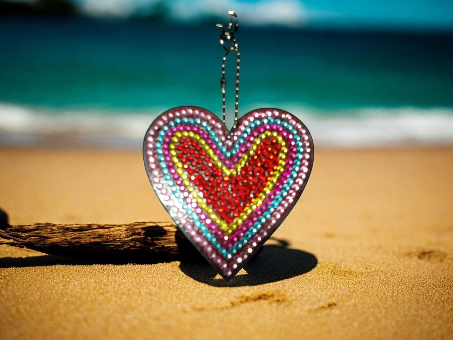 Red Center Heart Keychain with colorful beaded design hanging on beach sand