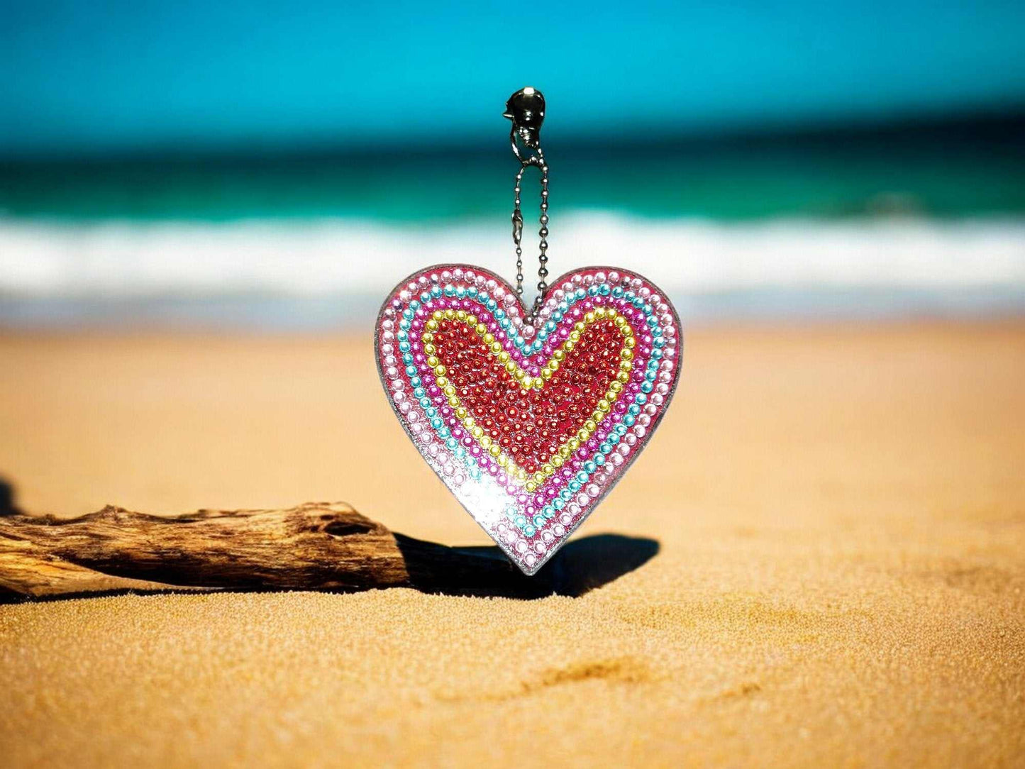 Red center heart keychain decorated with colorful beads on sandy beach background