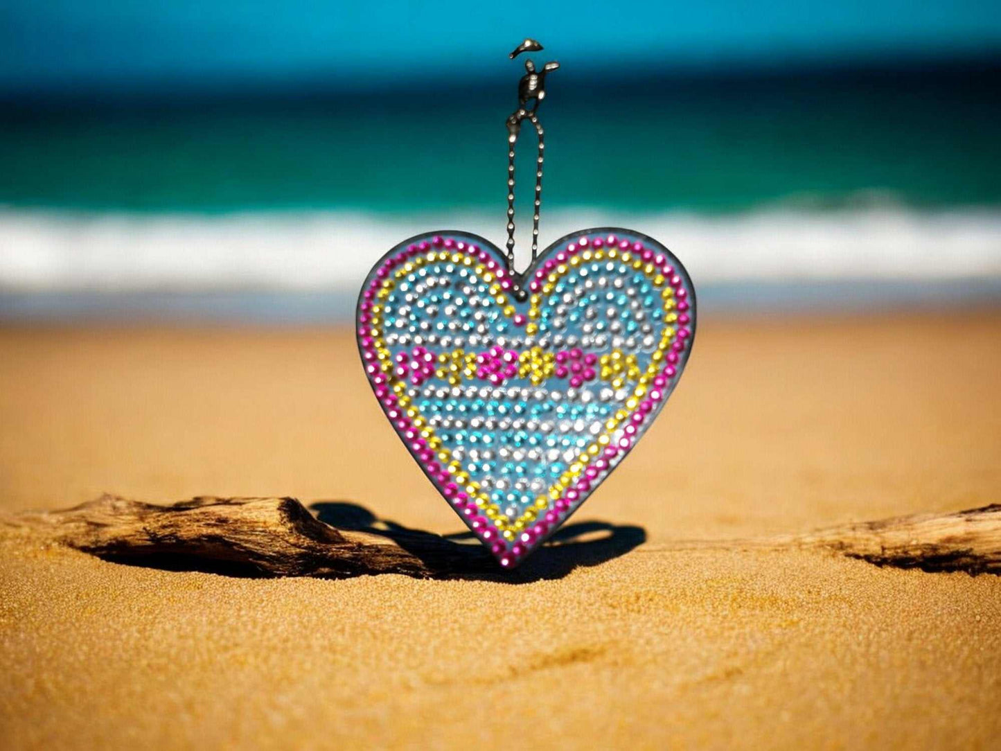 Blue heart-shaped keychain with flowers design on sandy beach background