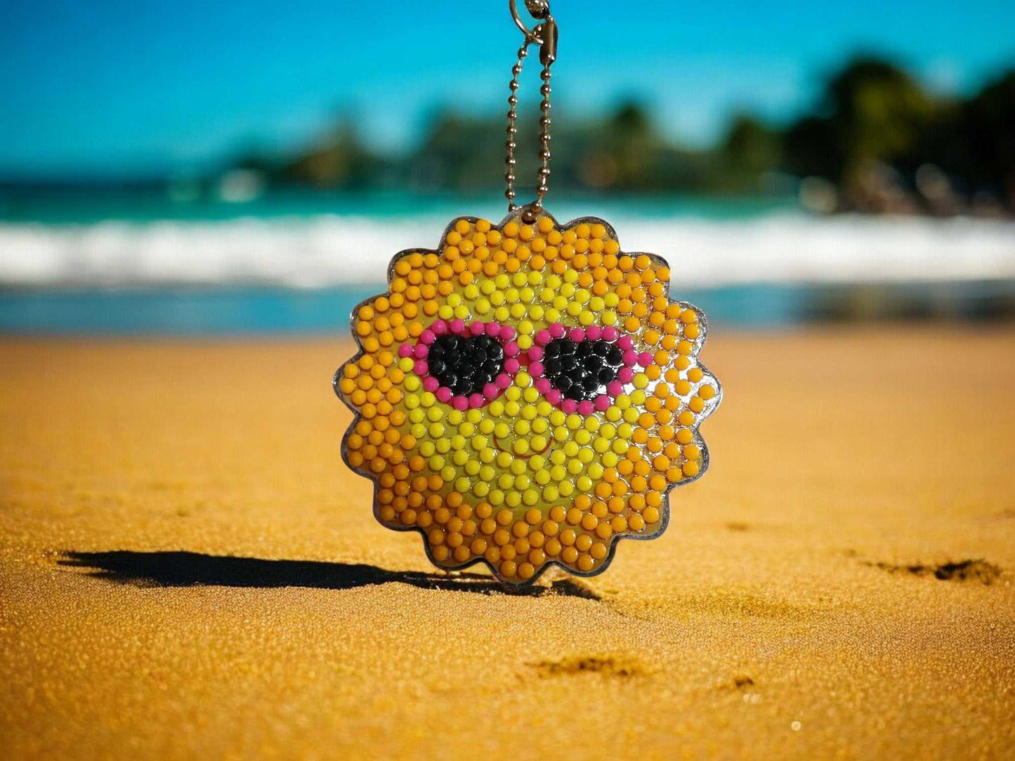 Keychain Sun with pink sunglasses keychain hanging on chain at the beach sand