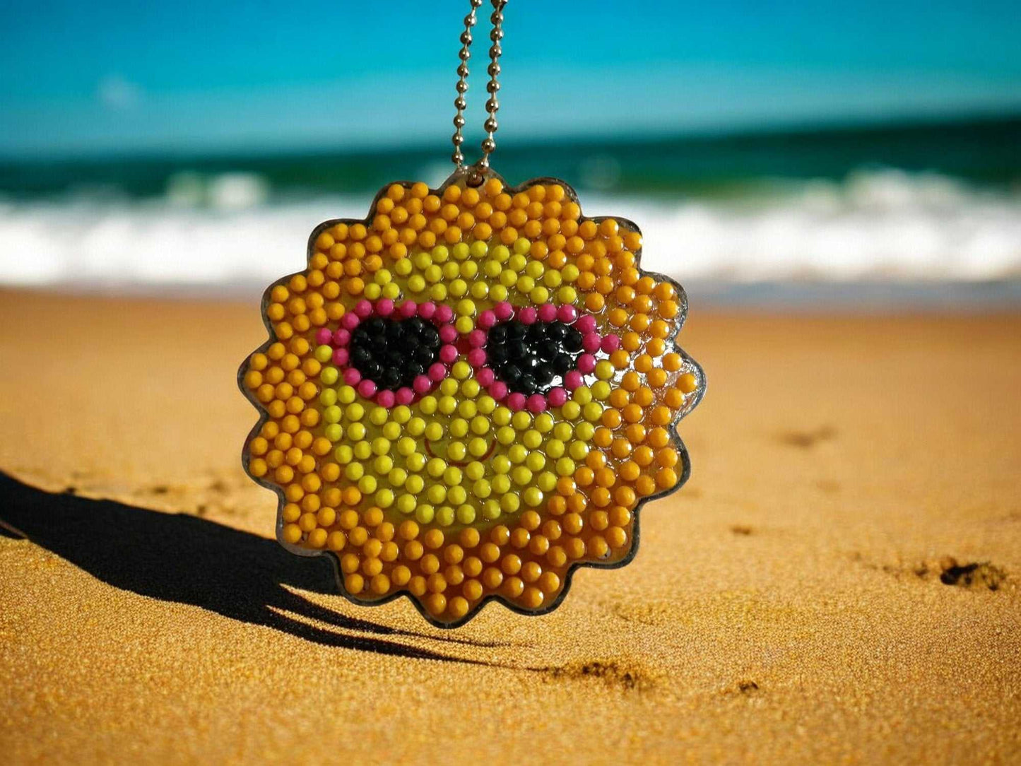 Keychain Sun w/Sunglasses keychain hanging on beach sand with ocean background