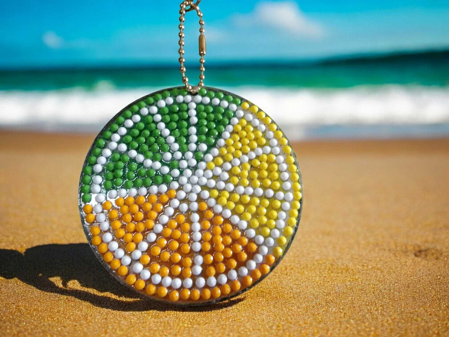 Colorful beaded citrus pie keychain with green, yellow, and orange segments on sandy beach background