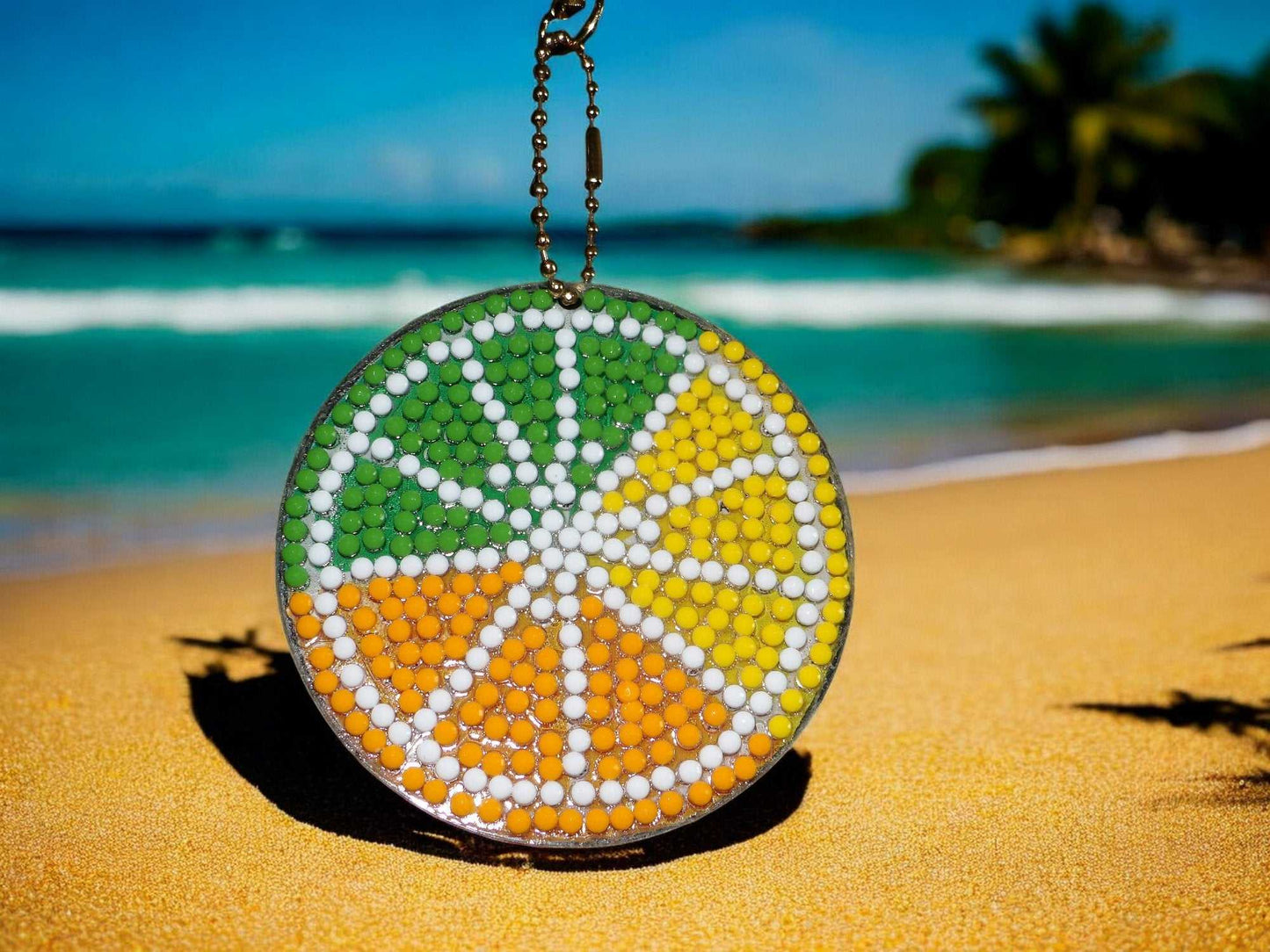 Colorful citrus pie keychain with green, yellow, and orange segments on sandy beach background