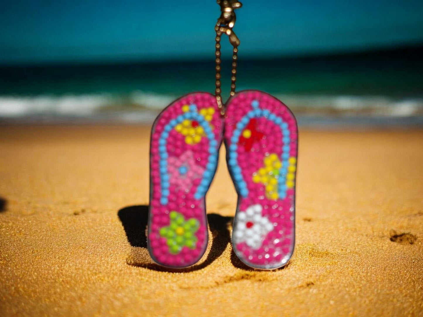 Pink beach sandals keychain with colorful floral design on sandy beach background
