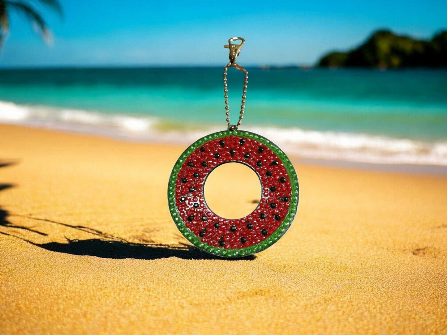 Watermelon keychain with green rind and red seeds on sandy beach background