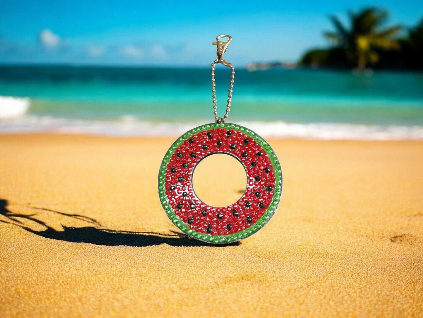 Watermelon keychain hanging on sandy beach with ocean background