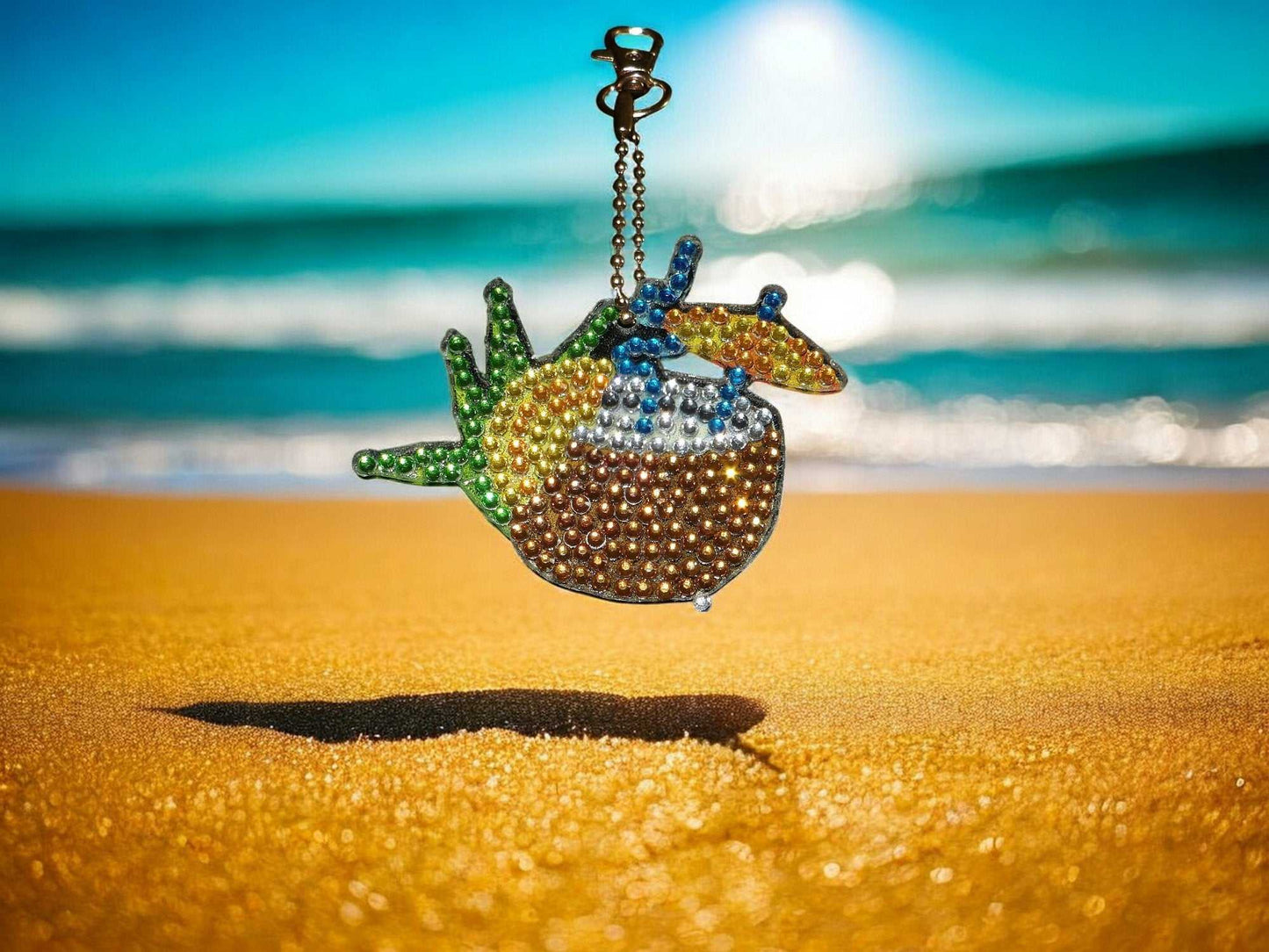 Summer drink with umbrella keychain hanging above beach sand with ocean background