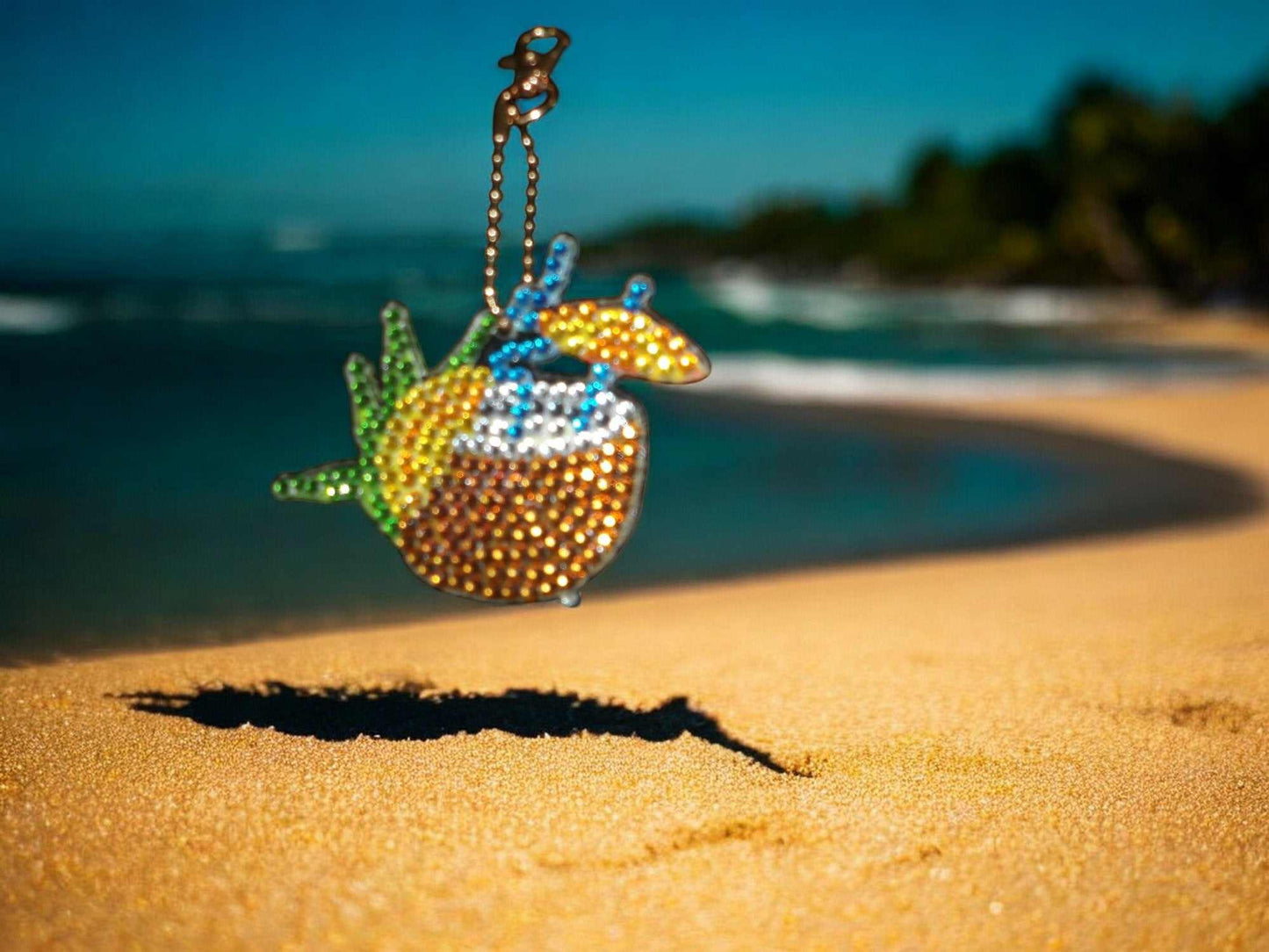 Colorful summer drink with umbrella keychain hanging over beach sand background