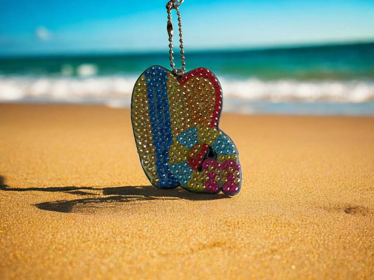 Surfs Up Surf Boads Keychain hanging on a chain on sandy beach with ocean background
