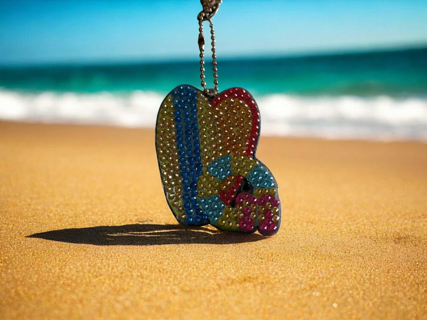 Surfs Up Surf Boards Keychain hanging on sandy beach with ocean background