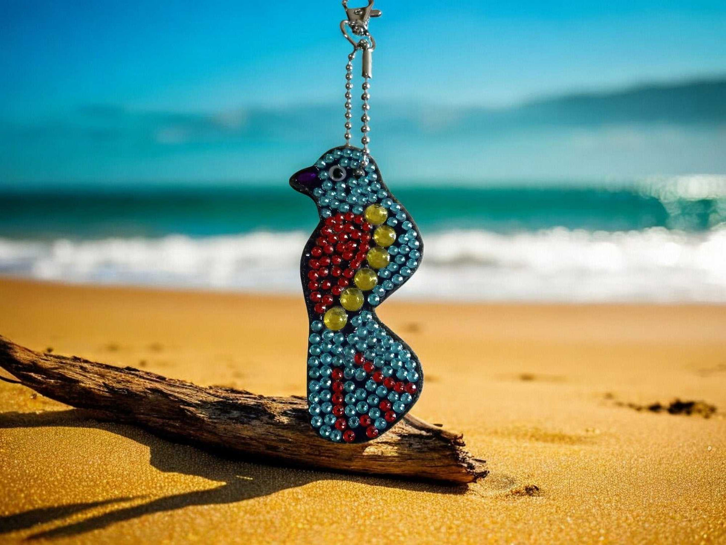 Blue and red bird keychain hanging on a driftwood piece at the beach with ocean background