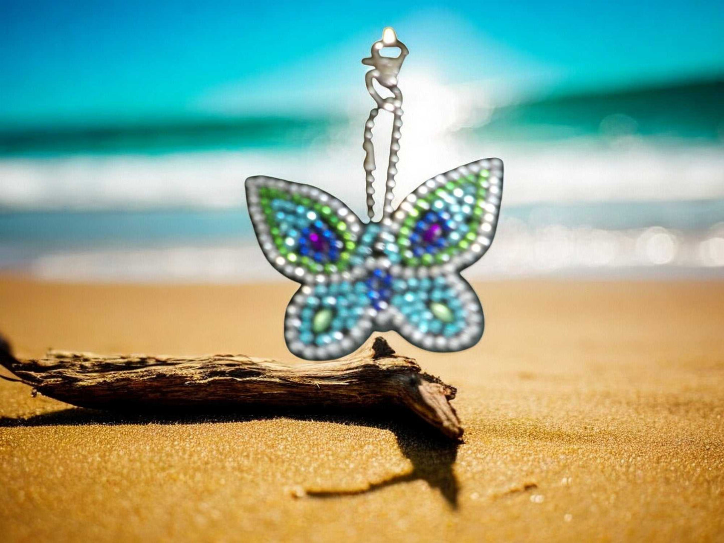 Colorful Blues Butterfly Keychain with sparkling beads hanging above sandy beach with ocean background