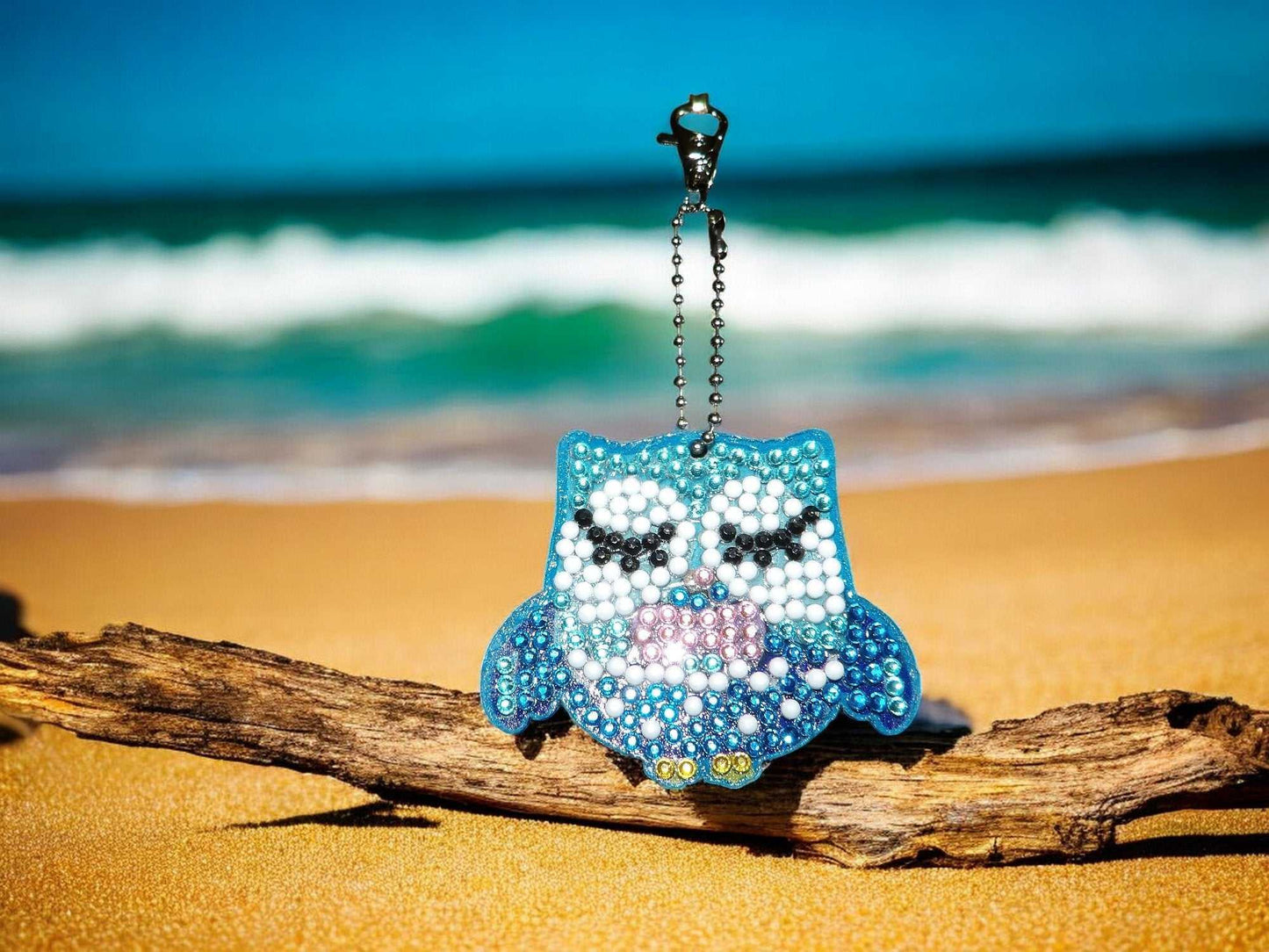 Blue & White Owl Keychain with beaded design hanging on a driftwood at the beach