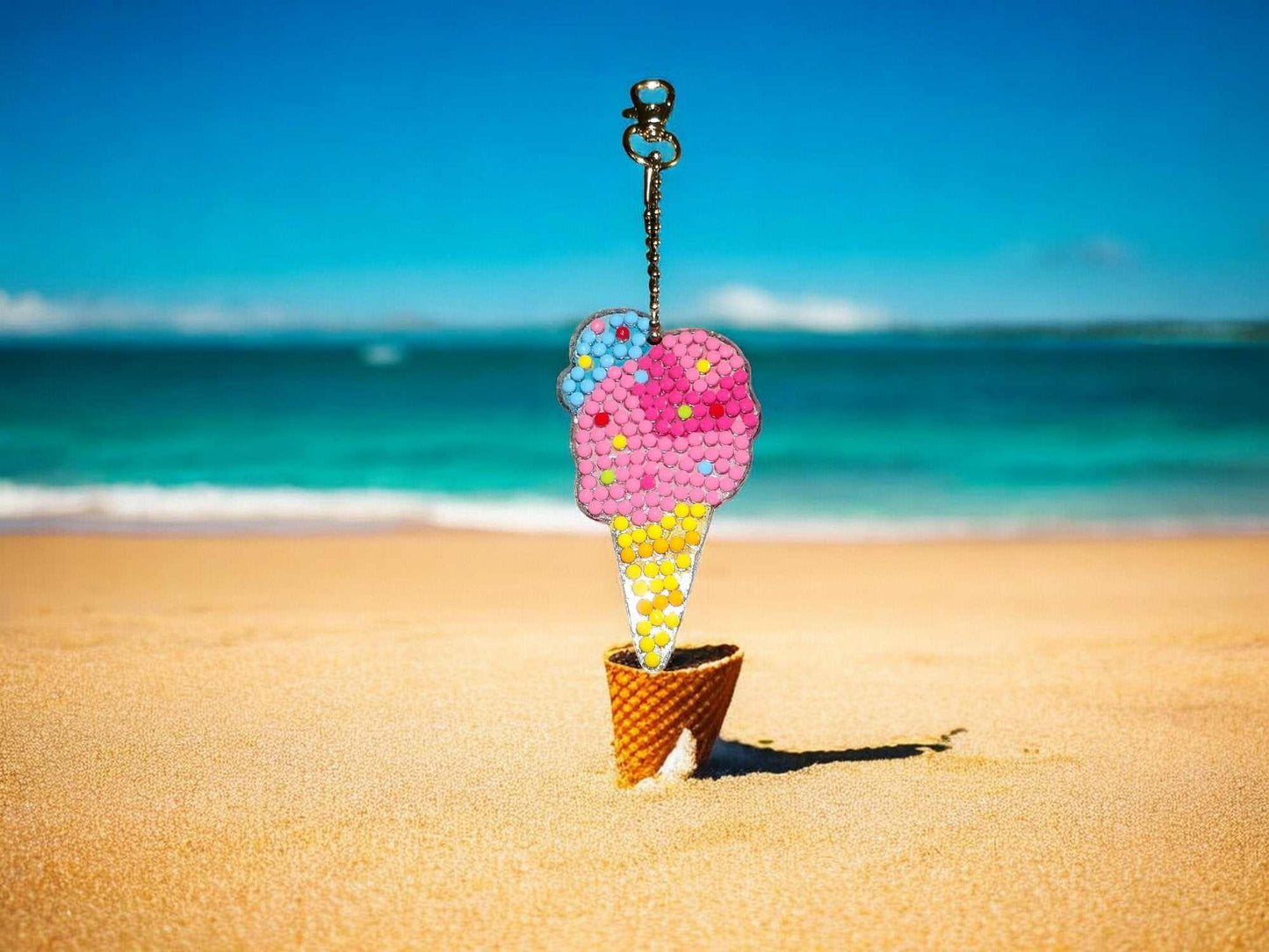 Colorful ice cream cone keychain on sandy beach with ocean background