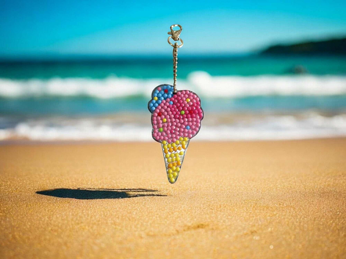 Colorful beaded ice cream cone keychain hanging on beach sand with ocean waves in background