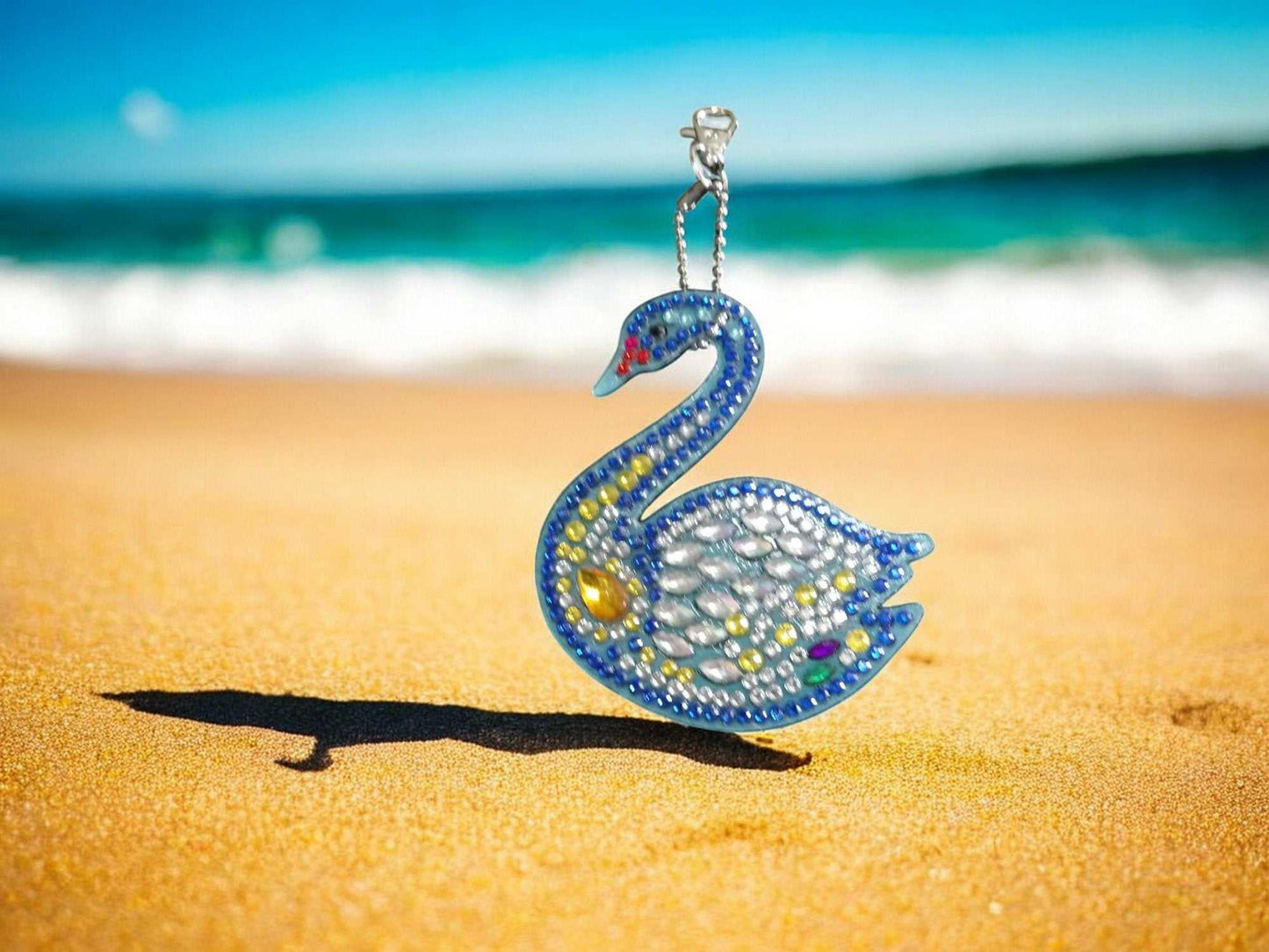 Swan shaped keychain adorned with yellow and multicolored crystals on a beach background