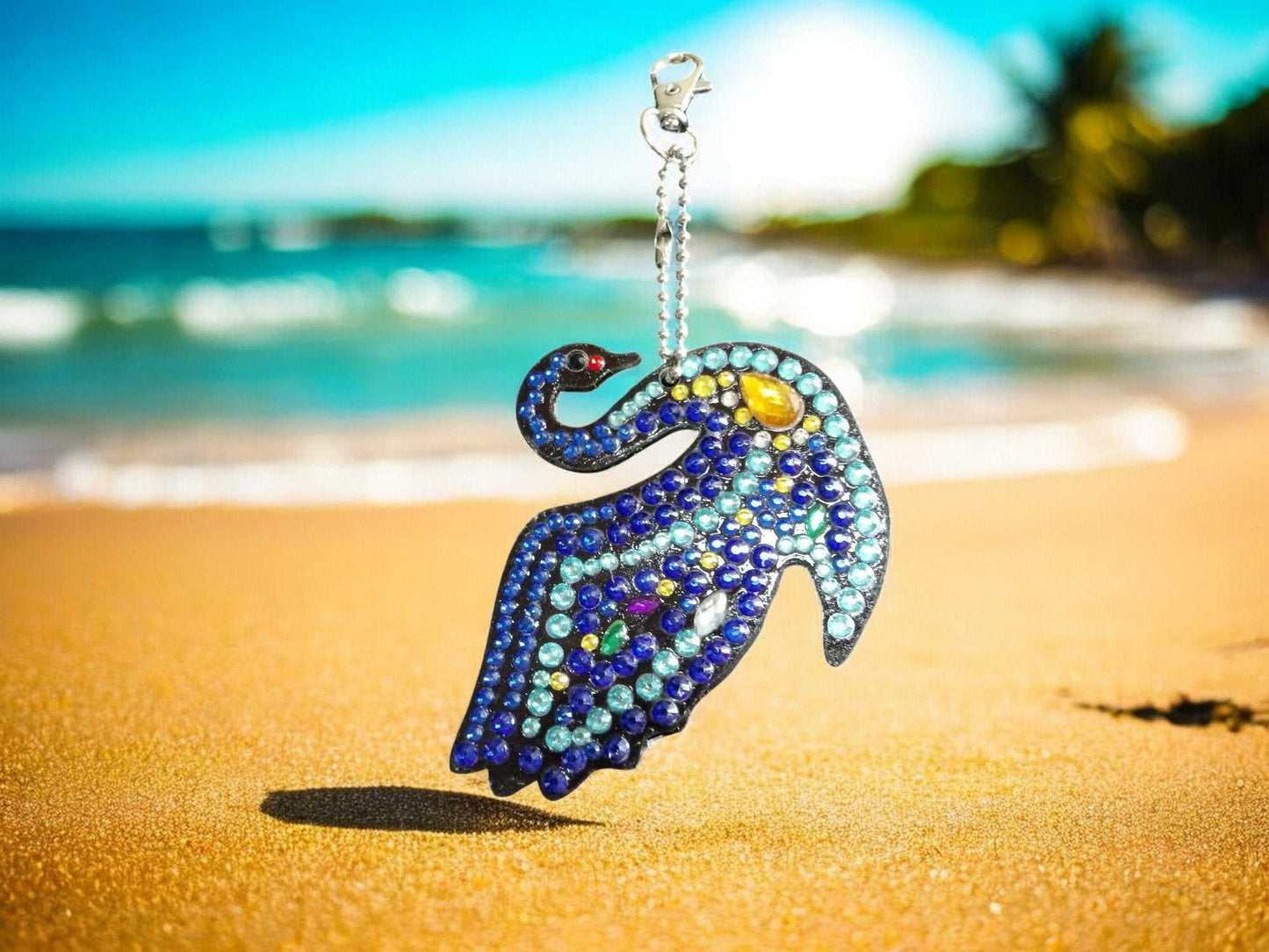 Multi-Blue Swan Keychain adorned with colorful gems on sandy beach background