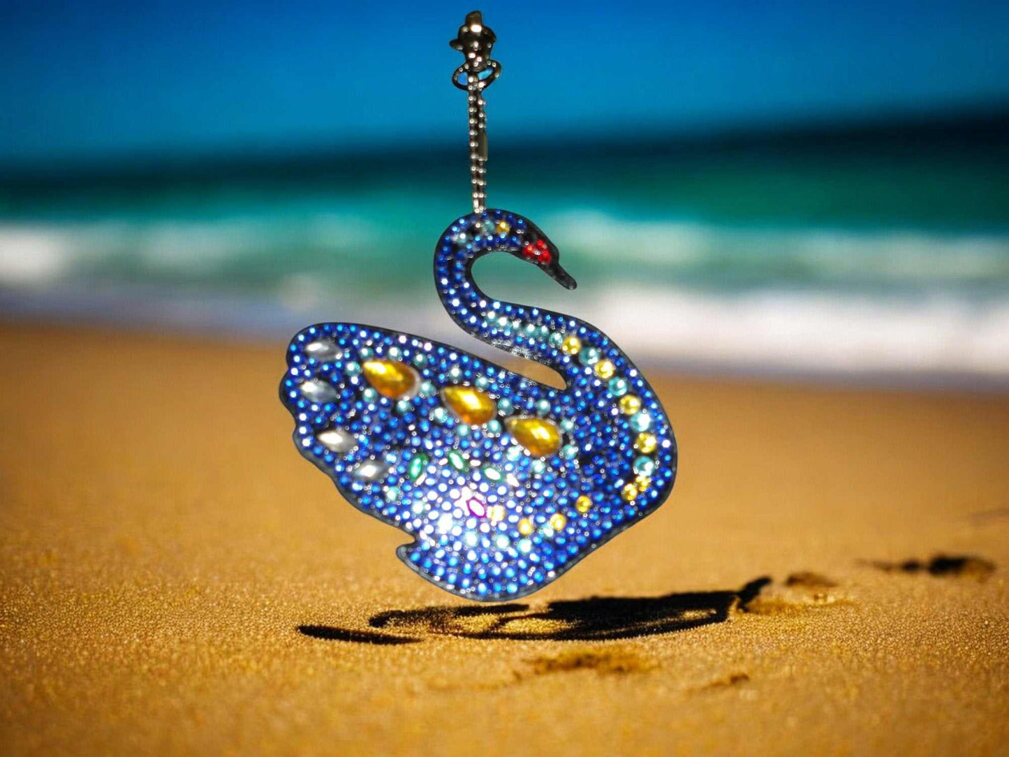 Dark blue yellow gem swan keychain with sparkling stones on sandy beach background