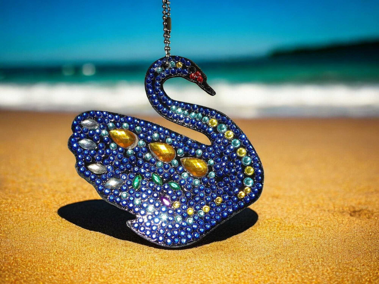 Dark blue swan keychain adorned with yellow gem and multicolored rhinestones on sandy beach background