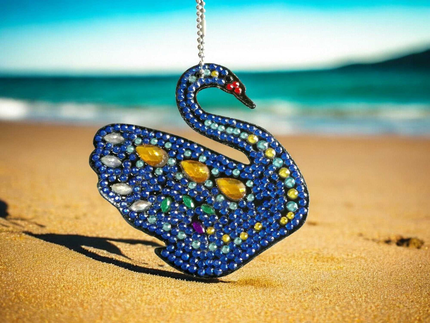 Dark blue swan keychain adorned with yellow and multicolored gems on sandy beach background