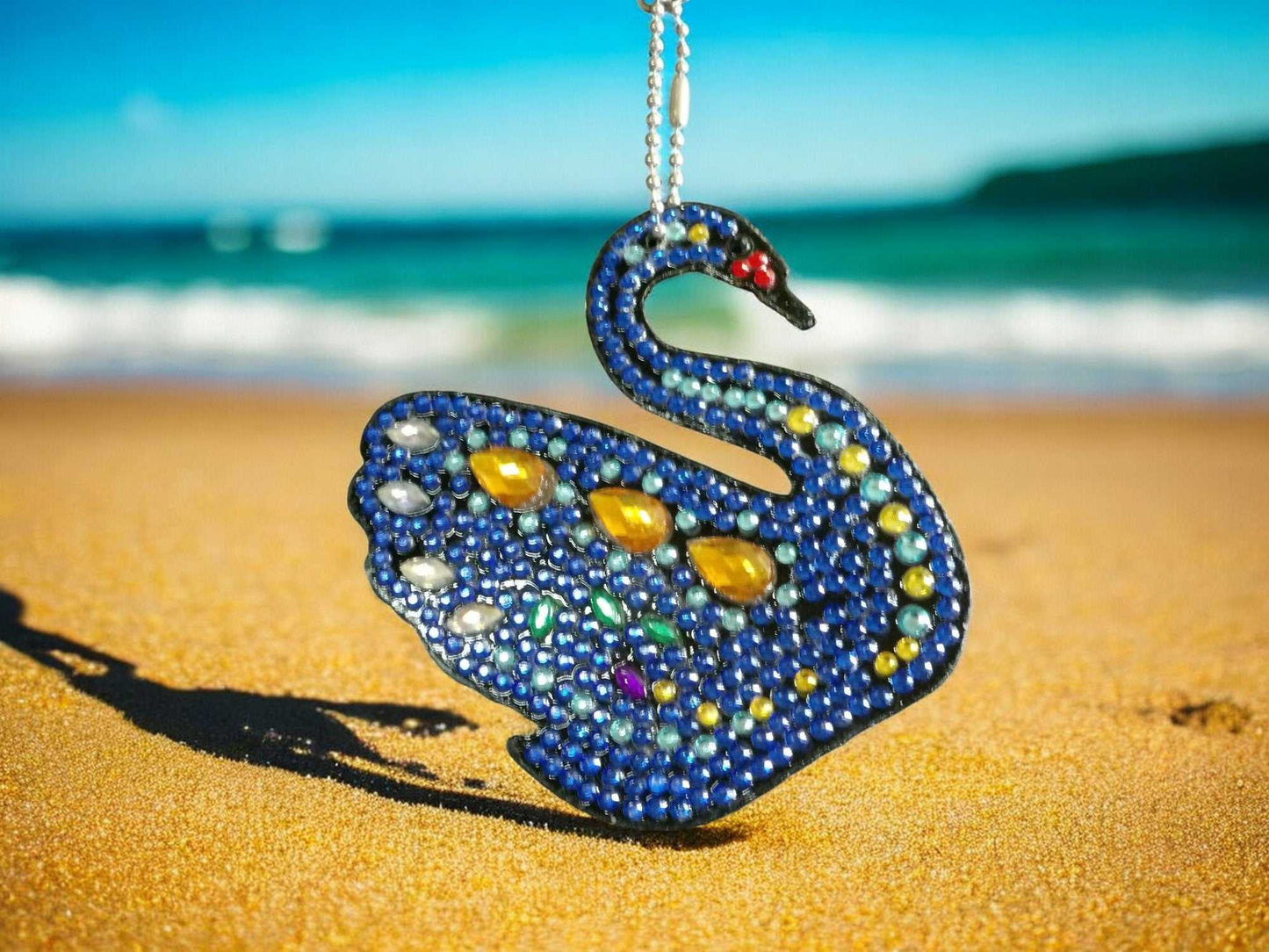 Dark blue swan-shaped keychain decorated with yellow and colorful gems on beach sand