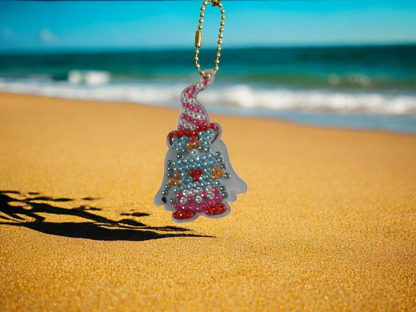 Capped Gnome Keychain hanging on a gold chain with beach and ocean background