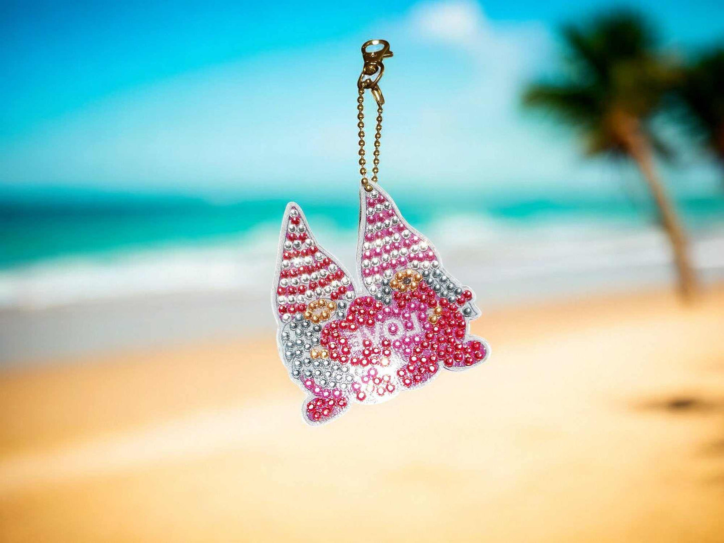 Gnomes In Love Keychain with pink and silver beads hanging by the beach background